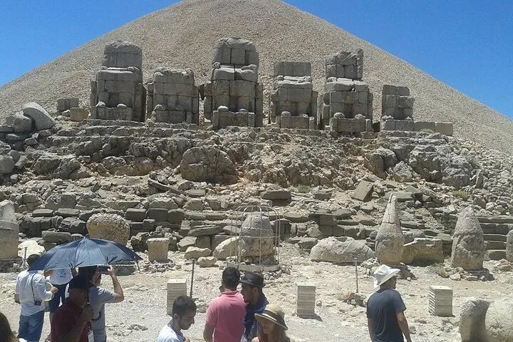 Travelers below the stone heads and the summit mound of Mount Nemrut on a Gobekli Tepe tour from Cappadocia, Turkey